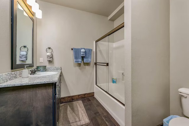 full bathroom with bath / shower combo with glass door, toilet, vanity, wood finished floors, and baseboards