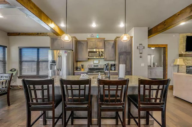 kitchen with appliances with stainless steel finishes, beamed ceiling, light stone counters, and wood finished floors