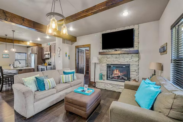 living area with dark wood-type flooring, beam ceiling, and a stone fireplace