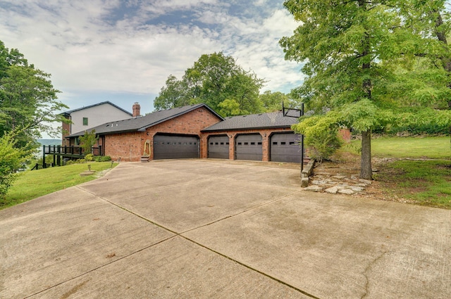 view of front of home with brick siding, concrete driveway, a chimney, an attached garage, and a front yard