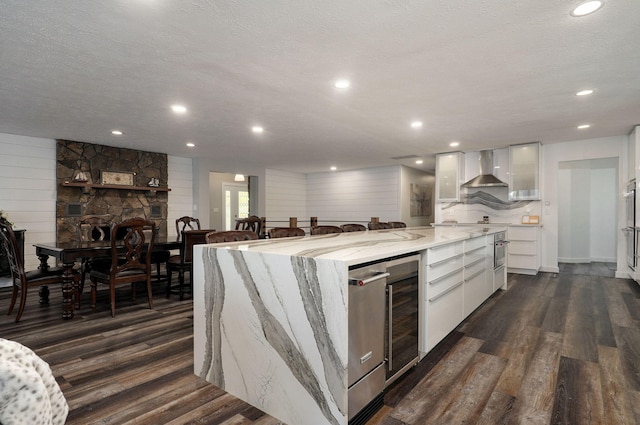 kitchen with wall chimney range hood, stainless steel oven, white cabinets, and dark wood-type flooring