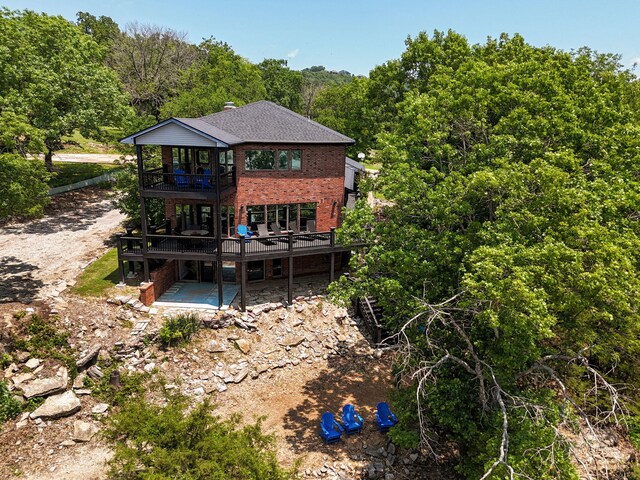 rear view of property featuring a patio, a balcony, brick siding, a shingled roof, and a view of trees