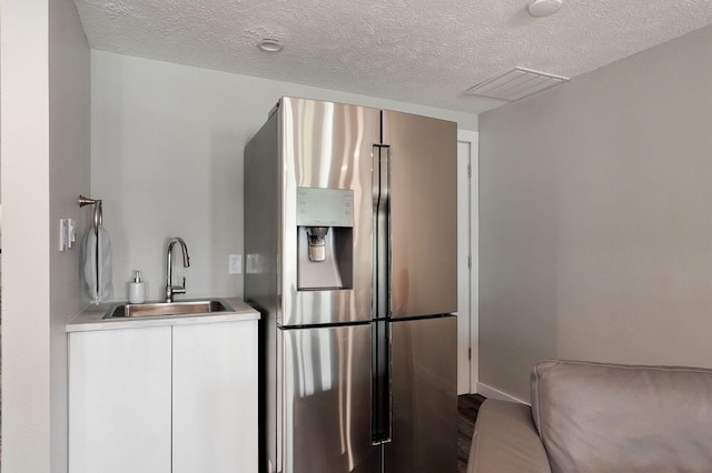 kitchen with light countertops, visible vents, white cabinetry, a sink, and stainless steel fridge