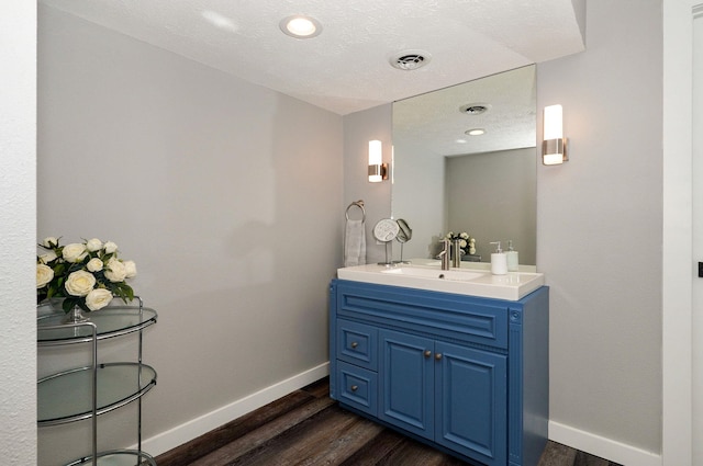 bathroom with visible vents, vanity, baseboards, and wood finished floors