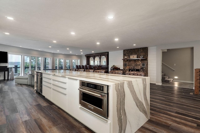 kitchen featuring dark wood-style flooring, white cabinets, stainless steel oven, and open floor plan