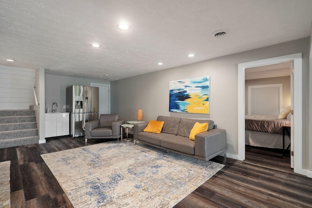 living room featuring dark wood-style floors, visible vents, a textured ceiling, and stairs