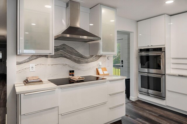 kitchen featuring black electric stovetop, light countertops, double oven, white cabinetry, and wall chimney range hood