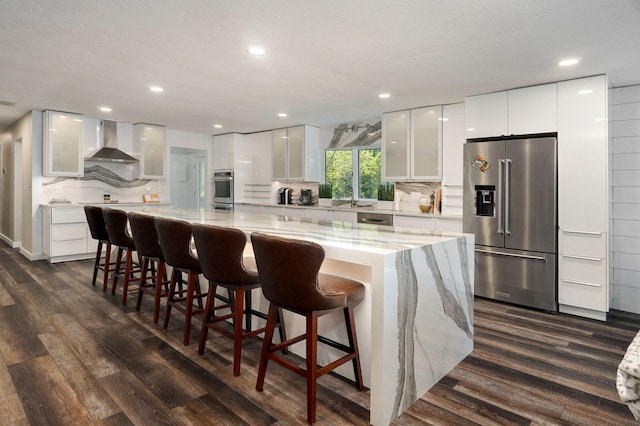 kitchen with wall chimney exhaust hood, appliances with stainless steel finishes, dark wood-style flooring, and backsplash