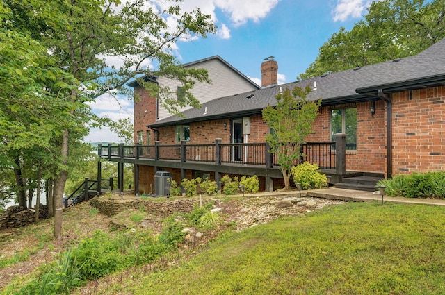 back of house with central AC unit, brick siding, a shingled roof, a lawn, and a chimney