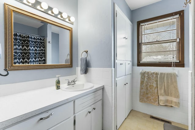 full bathroom with a wainscoted wall, visible vents, tile walls, and vanity