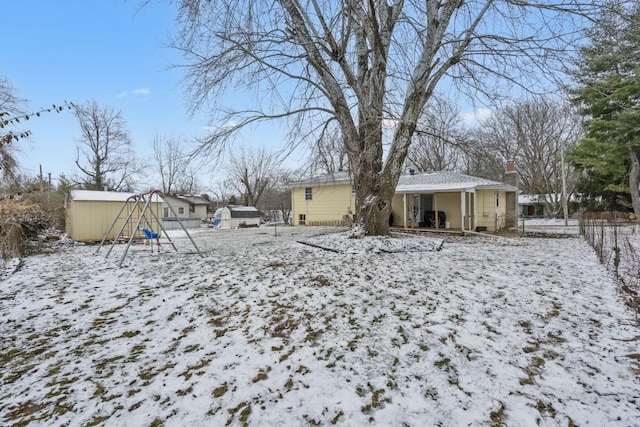 yard covered in snow with a storage shed, covered porch, a playground, and an outbuilding