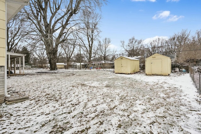 yard layered in snow with fence, a storage unit, and an outbuilding