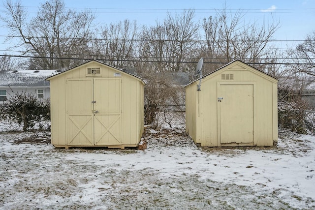 snow covered structure with a storage unit and an outbuilding