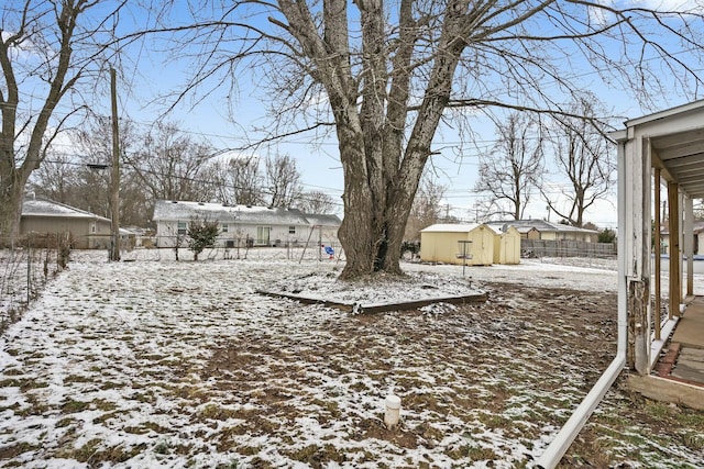 yard covered in snow with a storage unit, an outdoor structure, and fence