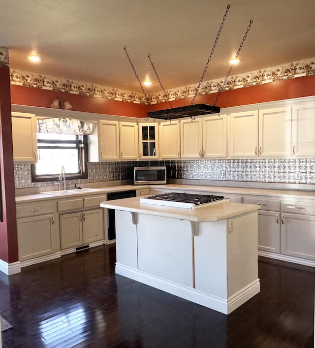 kitchen with cooktop, stainless steel microwave, dark wood-style flooring, light countertops, and a sink