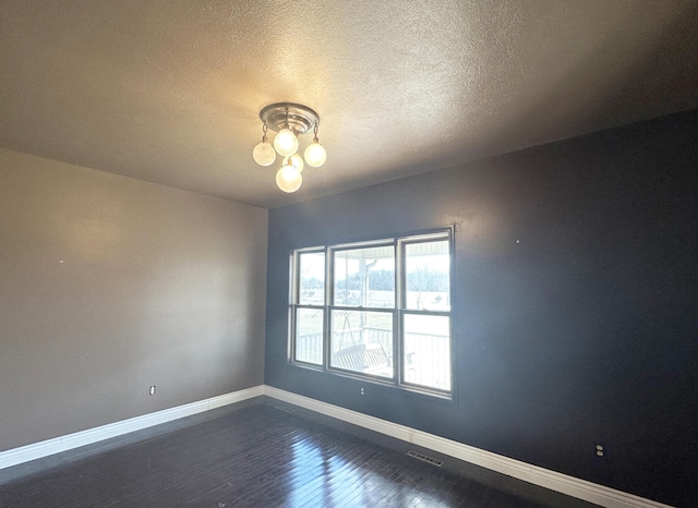 unfurnished room featuring a textured ceiling, dark wood-style flooring, visible vents, and baseboards