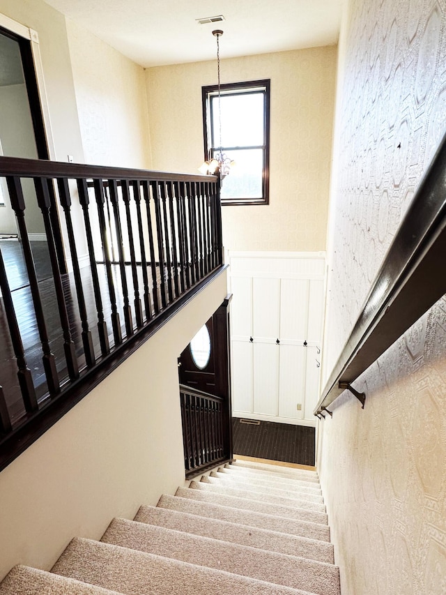 stairway with a wainscoted wall, visible vents, and a chandelier