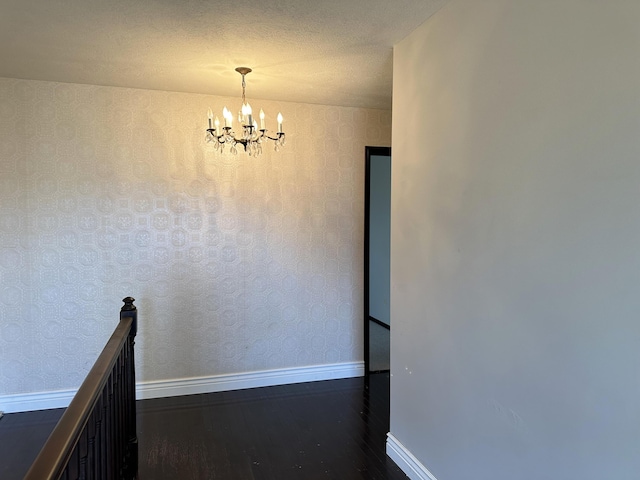 hallway featuring dark wood finished floors, a notable chandelier, a textured ceiling, baseboards, and wallpapered walls