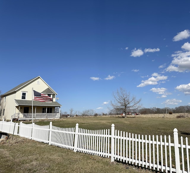 view of yard with a rural view, a fenced front yard, and covered porch