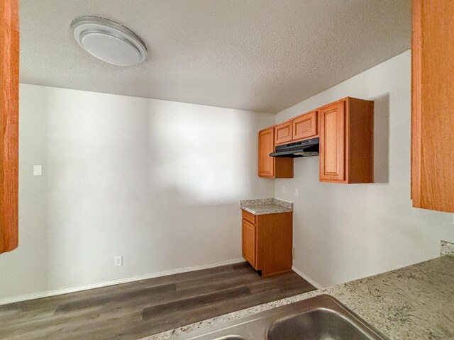 908 Jefferson Ave, Joplin, MO 64801 - kitchen featuring dark wood finished floors, light countertops, brown cabinetry, a textured ceiling, and under cabinet range hood