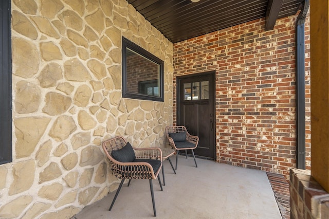 doorway to property featuring a porch, stone siding, and brick siding