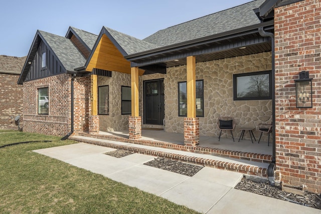 doorway to property featuring a shingled roof, stone siding, brick siding, and covered porch