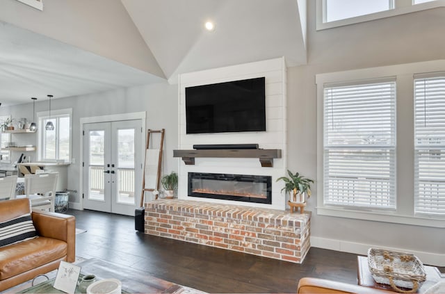 living area featuring baseboards, a glass covered fireplace, hardwood / wood-style floors, french doors, and high vaulted ceiling