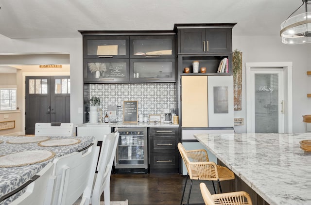 kitchen featuring beverage cooler, dark wood-style floors, glass insert cabinets, light stone counters, and backsplash