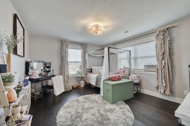 bedroom with a textured ceiling, wood finished floors, visible vents, and baseboards