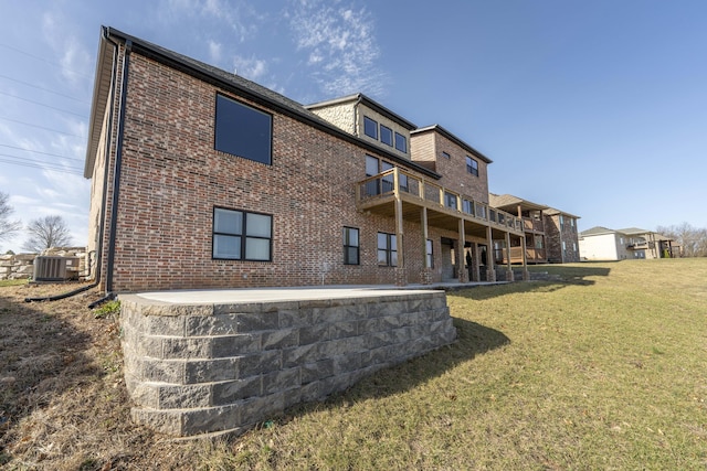 back of property with brick siding, a yard, central AC unit, a patio area, and a balcony