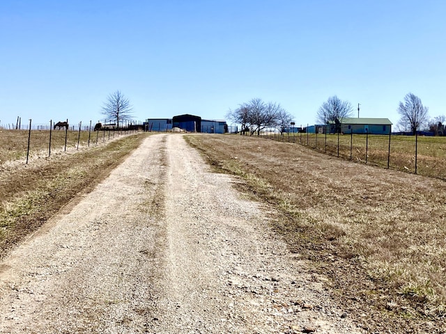 view of road with dirt driveway and a rural view