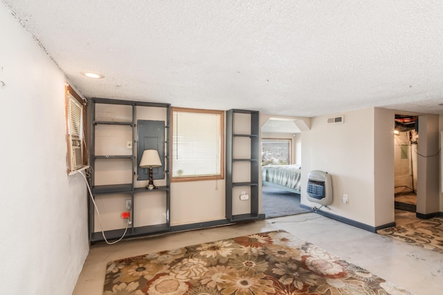 interior space featuring baseboards, visible vents, heating unit, a textured ceiling, and concrete flooring