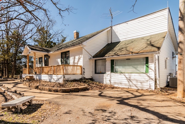 view of front of property with a porch, a chimney, a shingled roof, and central air condition unit