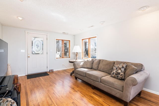 living room featuring light wood-style flooring, visible vents, baseboards, and a textured ceiling