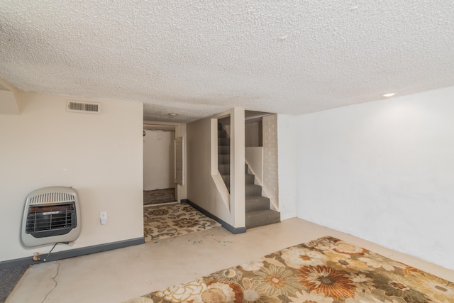 finished below grade area with visible vents, a textured ceiling, heating unit, and stairs