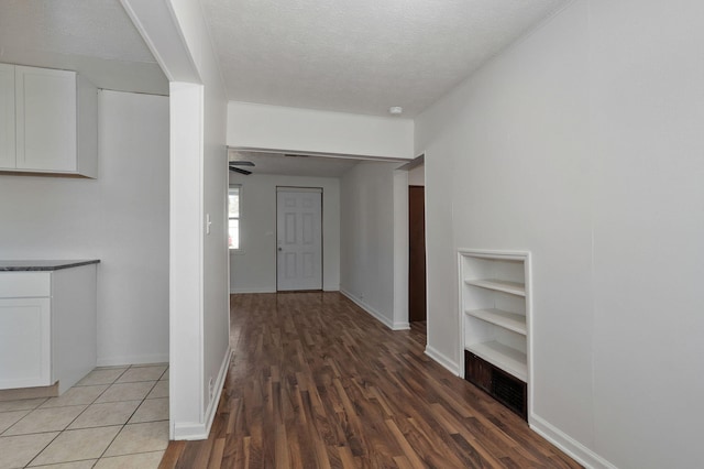 hall with built in shelves, baseboards, a textured ceiling, and wood finished floors