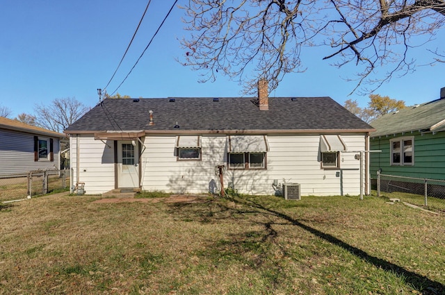 rear view of house with a yard, central AC unit, a shingled roof, and fence