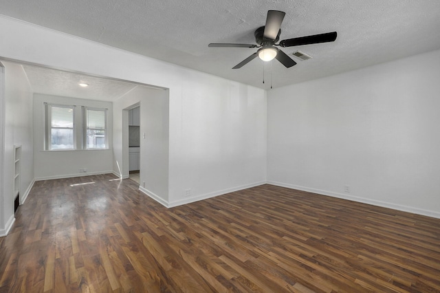 empty room with a textured ceiling, dark wood-type flooring, visible vents, and baseboards