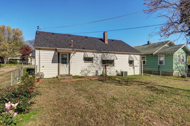 rear view of house with cooling unit, fence, a yard, roof with shingles, and a chimney