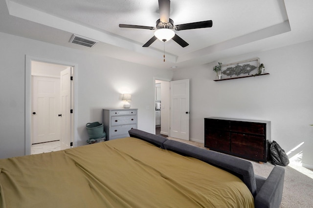 carpeted bedroom featuring a ceiling fan, a tray ceiling, visible vents, and baseboards