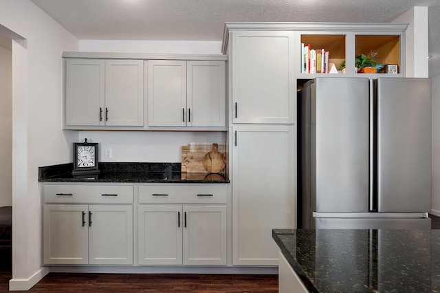 kitchen with freestanding refrigerator, dark wood-style flooring, a textured ceiling, and dark stone countertops