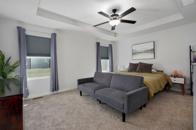 carpeted bedroom featuring a tray ceiling, visible vents, and baseboards
