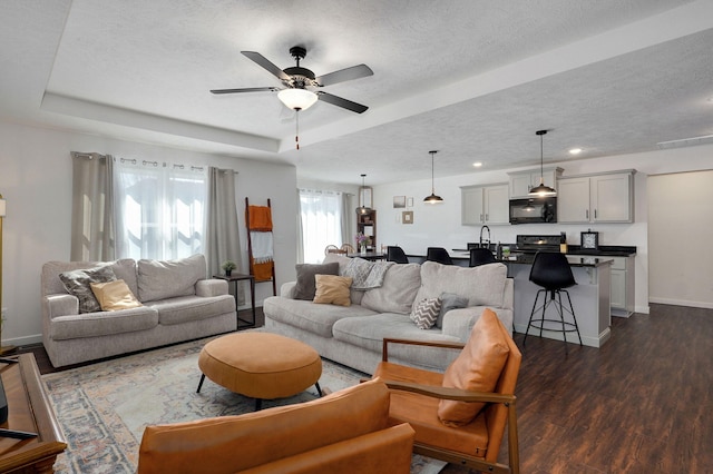 living area featuring a raised ceiling, dark wood finished floors, a textured ceiling, and baseboards