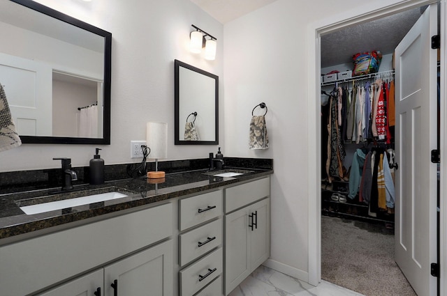 full bath with a walk in closet, marble finish floor, a sink, and double vanity