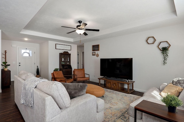 living area with a tray ceiling, dark wood finished floors, baseboards, and ceiling fan