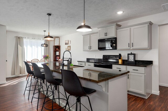 kitchen with an island with sink, black appliances, dark wood-style flooring, and a sink