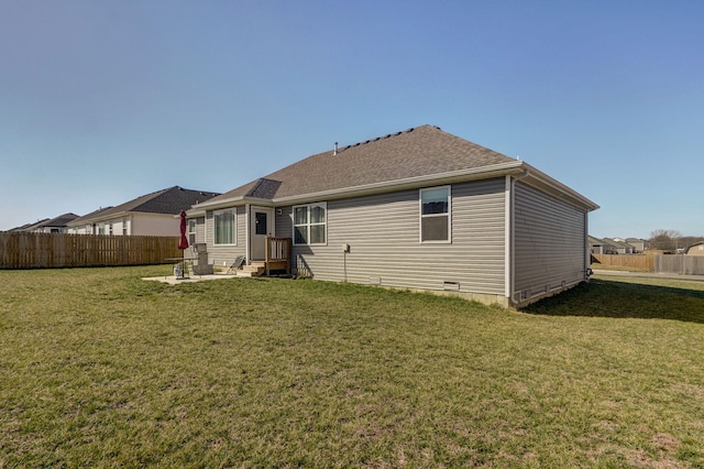 rear view of property featuring crawl space, a shingled roof, fence, and a lawn
