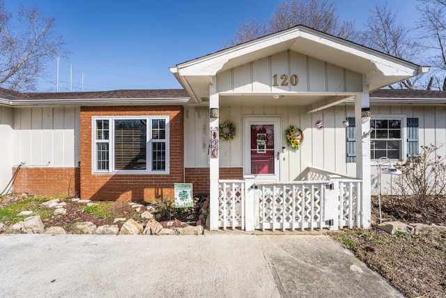 entrance to property featuring board and batten siding, brick siding, a porch, and roof with shingles