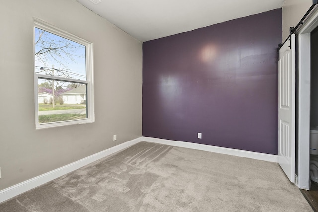 carpeted empty room featuring baseboards and a barn door
