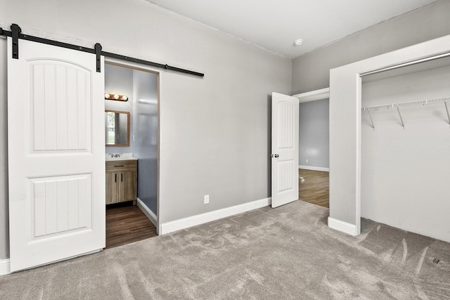 unfurnished bedroom featuring carpet, baseboards, ensuite bath, a barn door, and a closet